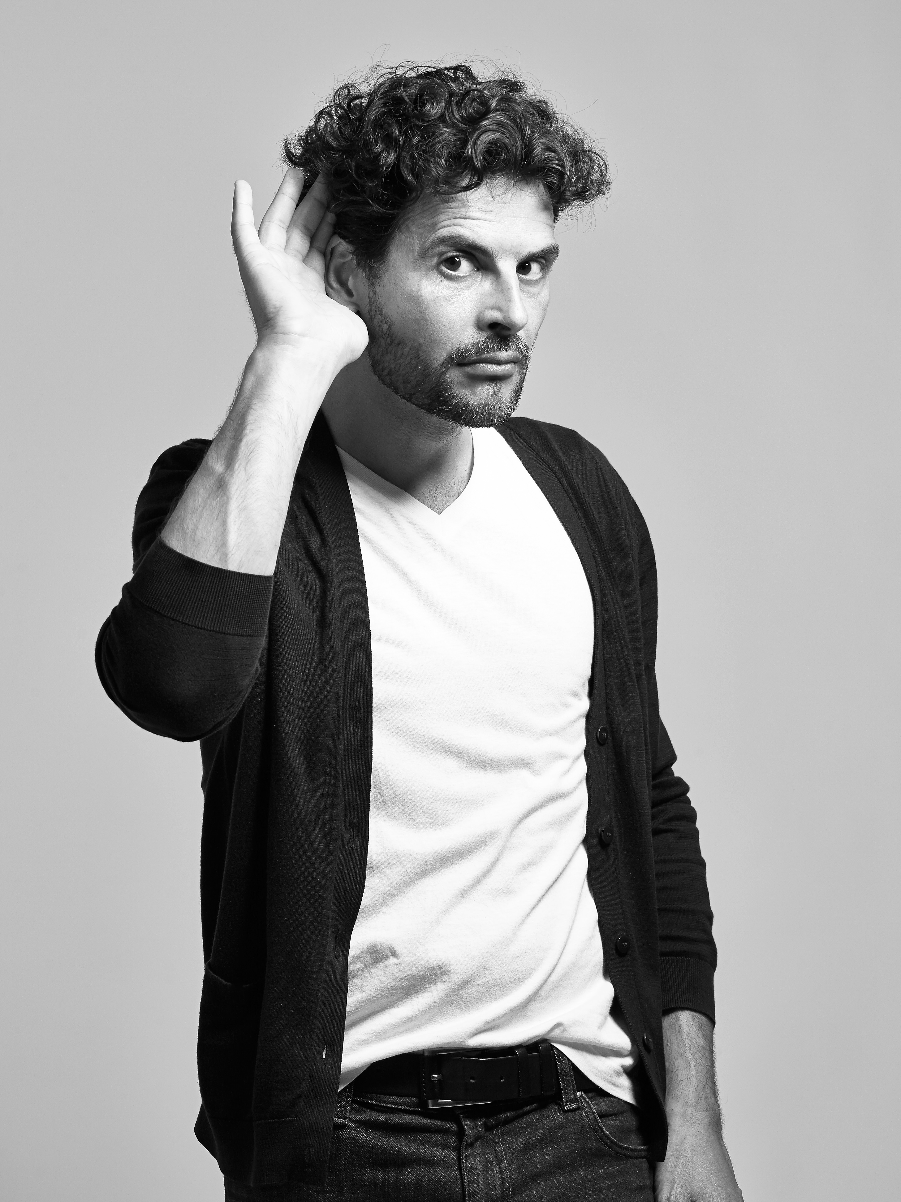 BW portrait of a curly-haired italian man holding his hand at his ear to say 